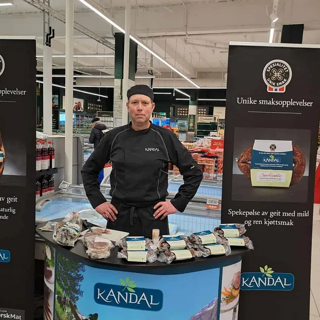 Mann i Kandal-uniform bak stand med spekemat i daglegvarebutikk.