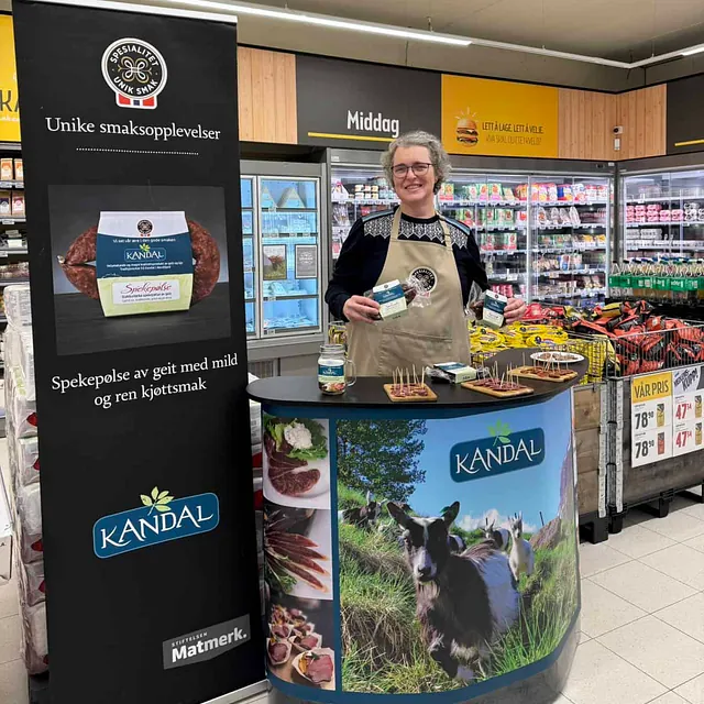 Kvinne bak Kandal-stand i butikk som held produkt og smiler framfor banner.
