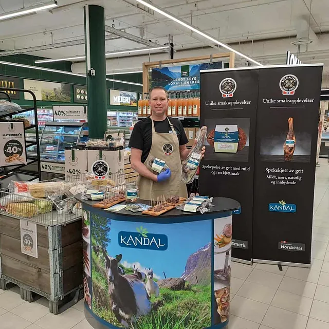 Mann bak Kandal-stand i butikk med spekekjøt og plakatar.